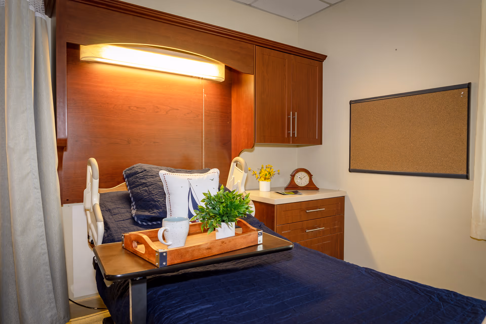 Bedroom in a senior facility with navy bedding, wood cabinets, and a bedside tray.