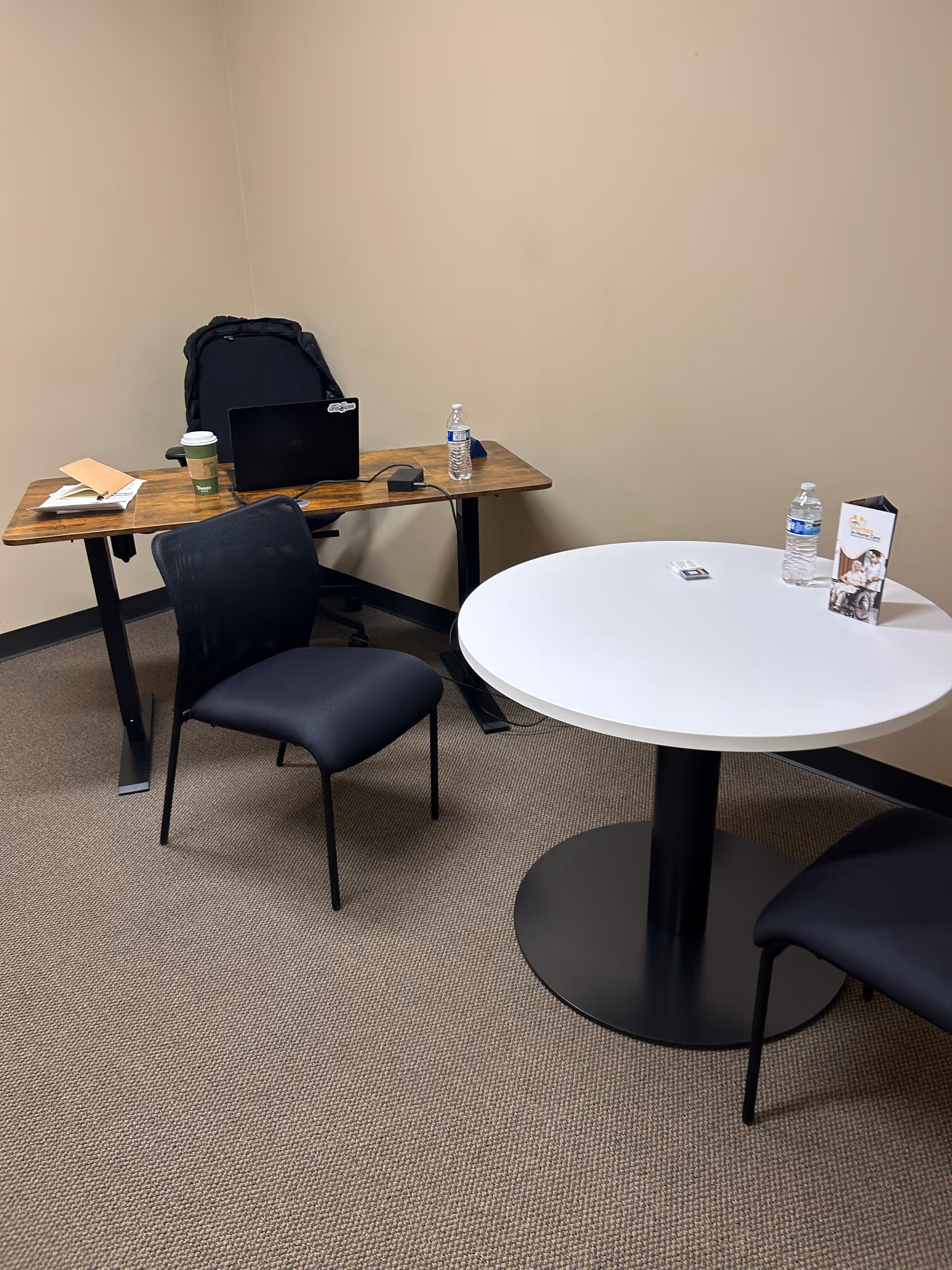 Interior workspace with a wooden desk, laptop, and a round table with chairs.