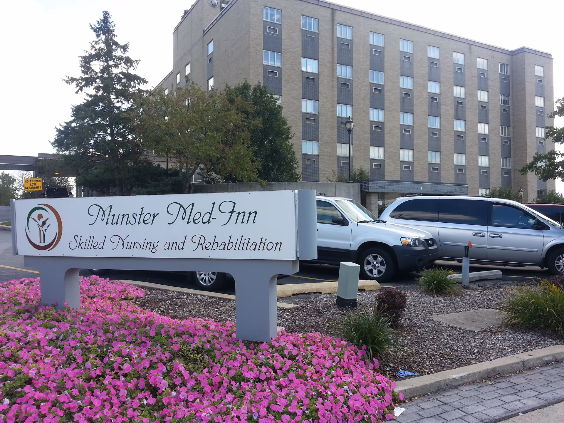 Exterior view of Munster Med-Inn building with sign and pink flowers in front.