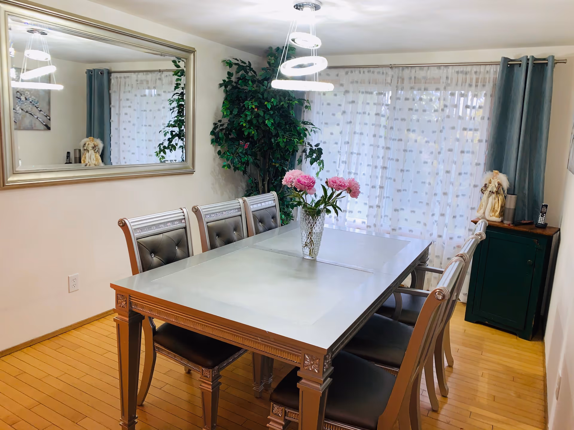 Dining room with a long glass table, upholstered chairs, a mirror, and pink flower centerpiece.