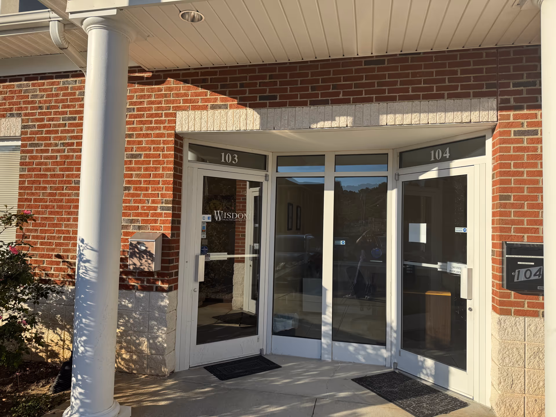 Brick building entrance with glass double doors labeled 103/104, Wisdom Senior Care Franchise