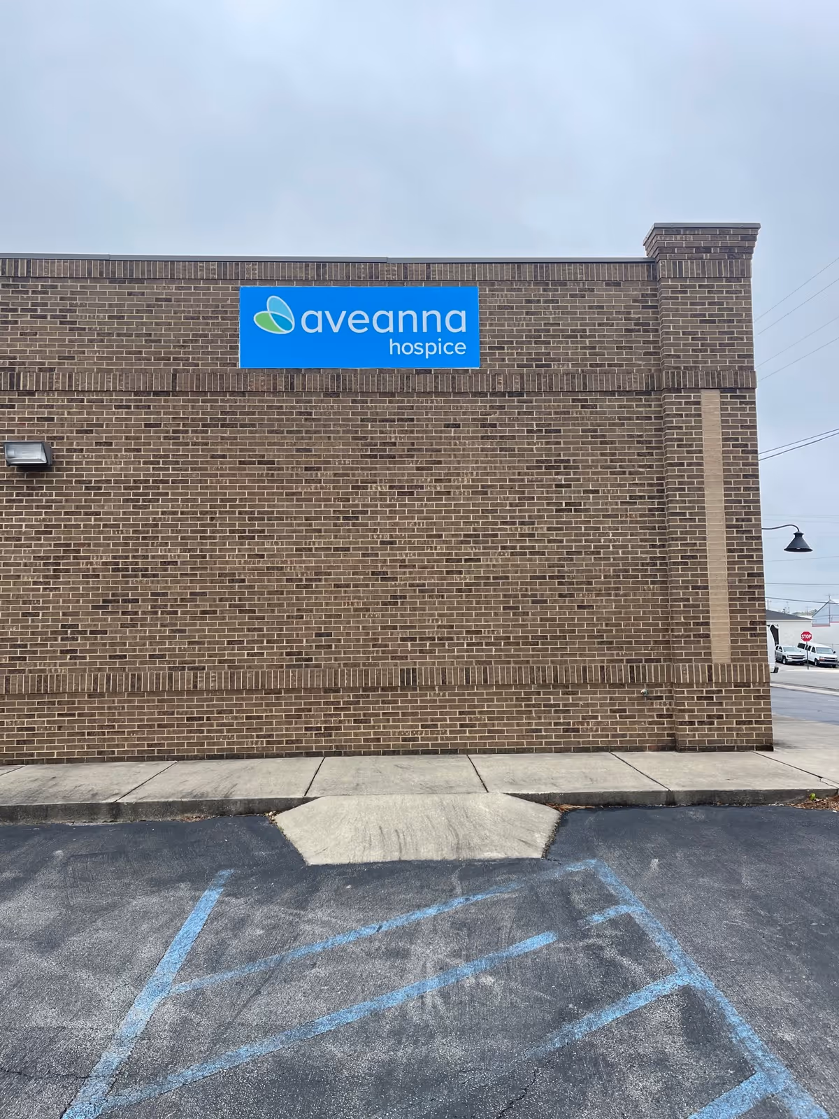 Brick building with Aveanna Hospice sign on the front and adjacent parking.