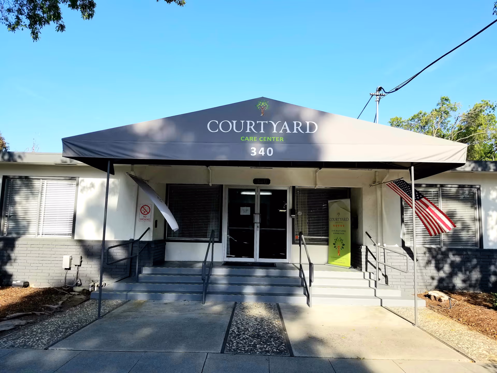 Front entrance of Courtyard Care Center with awning, steps, and flag.