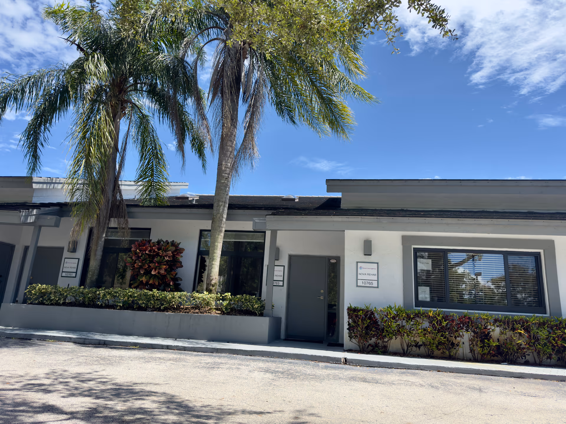Front view of a senior living facility with palm trees and a sign near the entrance.