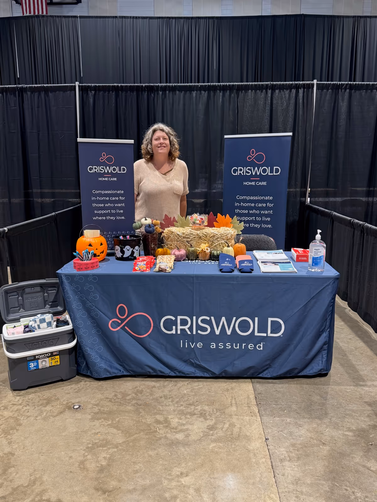 A Griswold Home Care booth with banners and a standing woman behind a decorated table.