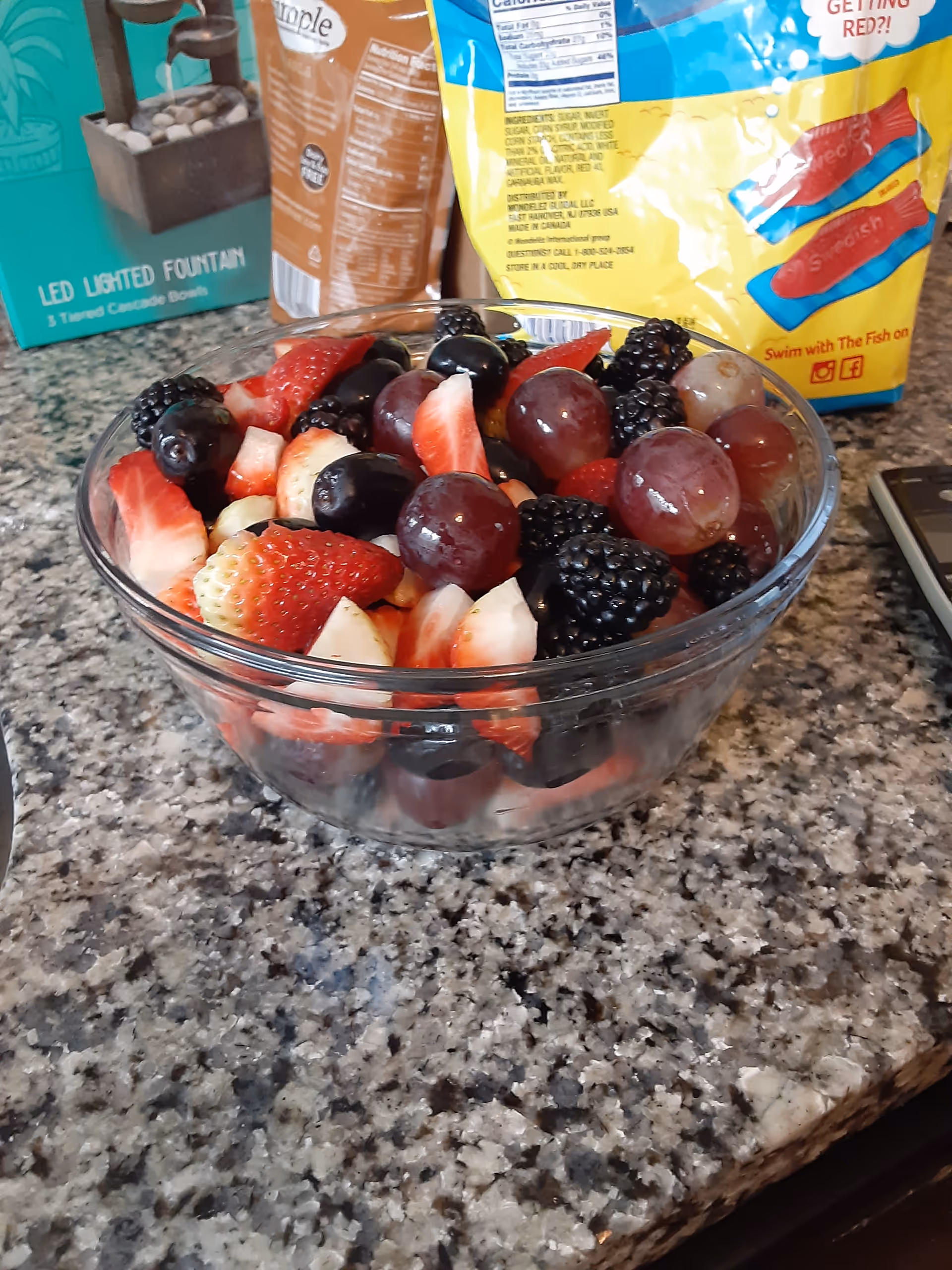 Glass bowl of mixed berries on a granite kitchen counter with snack bags behind.