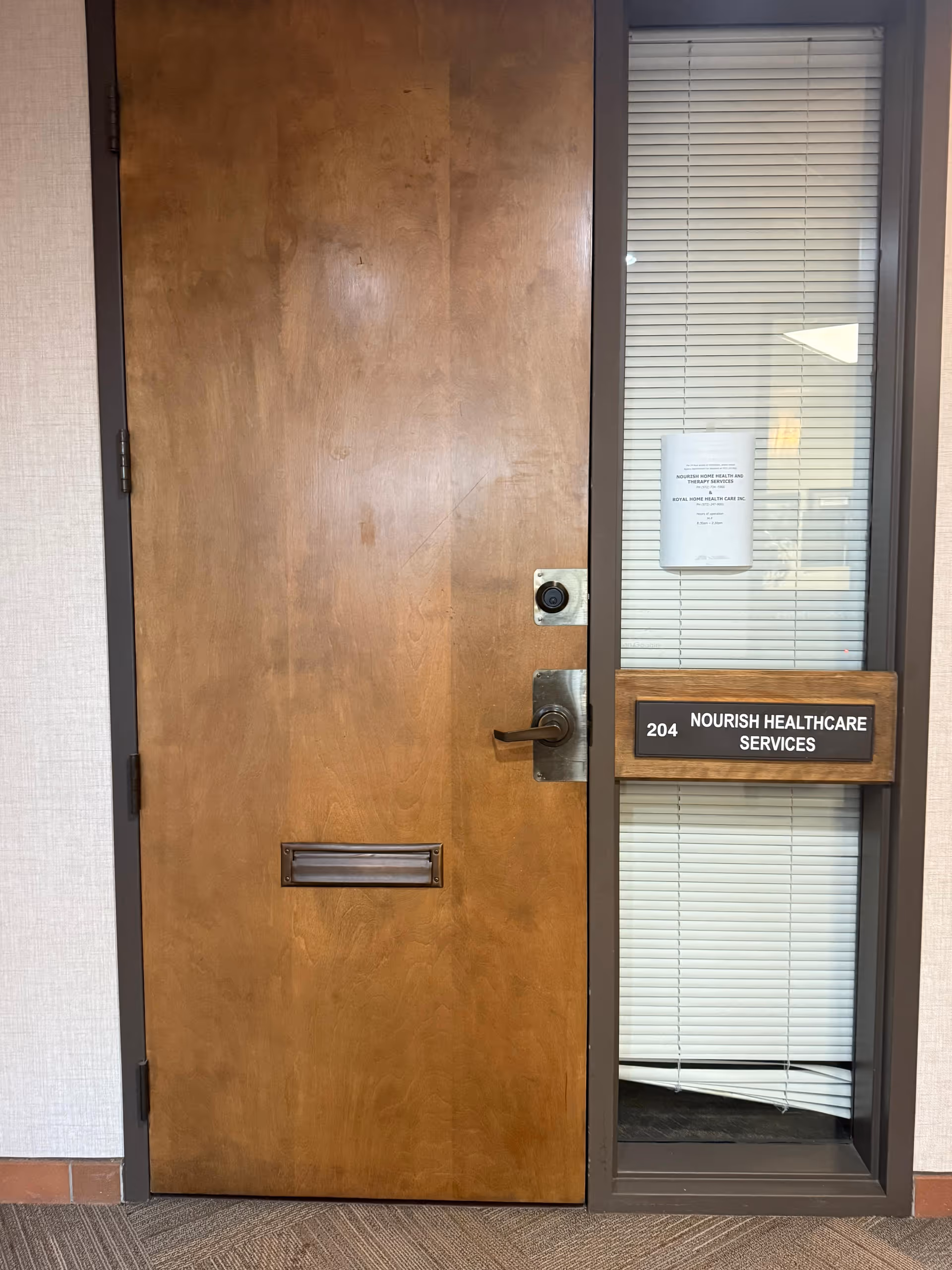 Wooden door with mail slot beside a glass panel displaying Nourish Healthcare Services in a hallway.