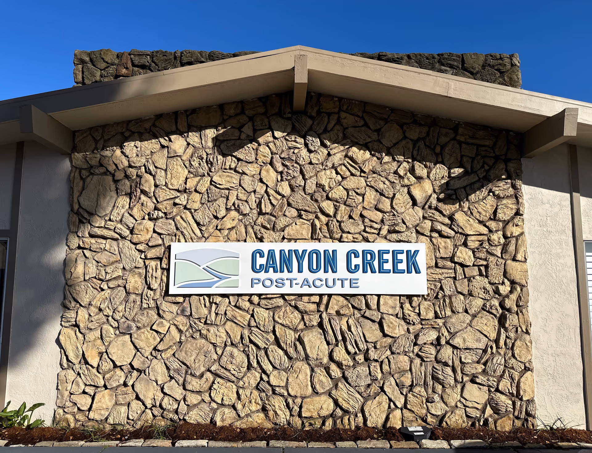 Stone building exterior with a Canyon Creek Post-Acute sign mounted on the wall