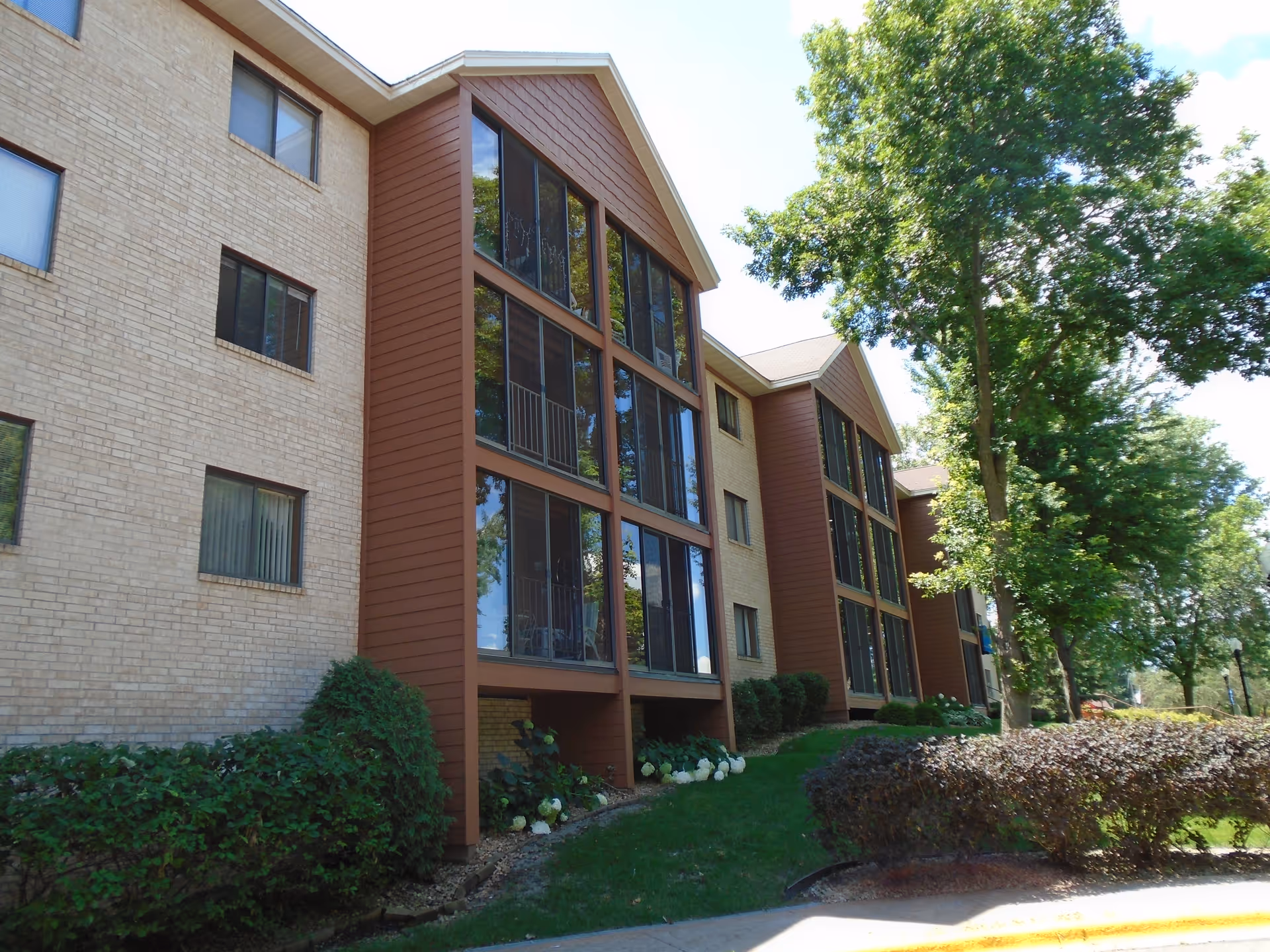 Three-story brick senior living building with brown panel accents and large glass windows.