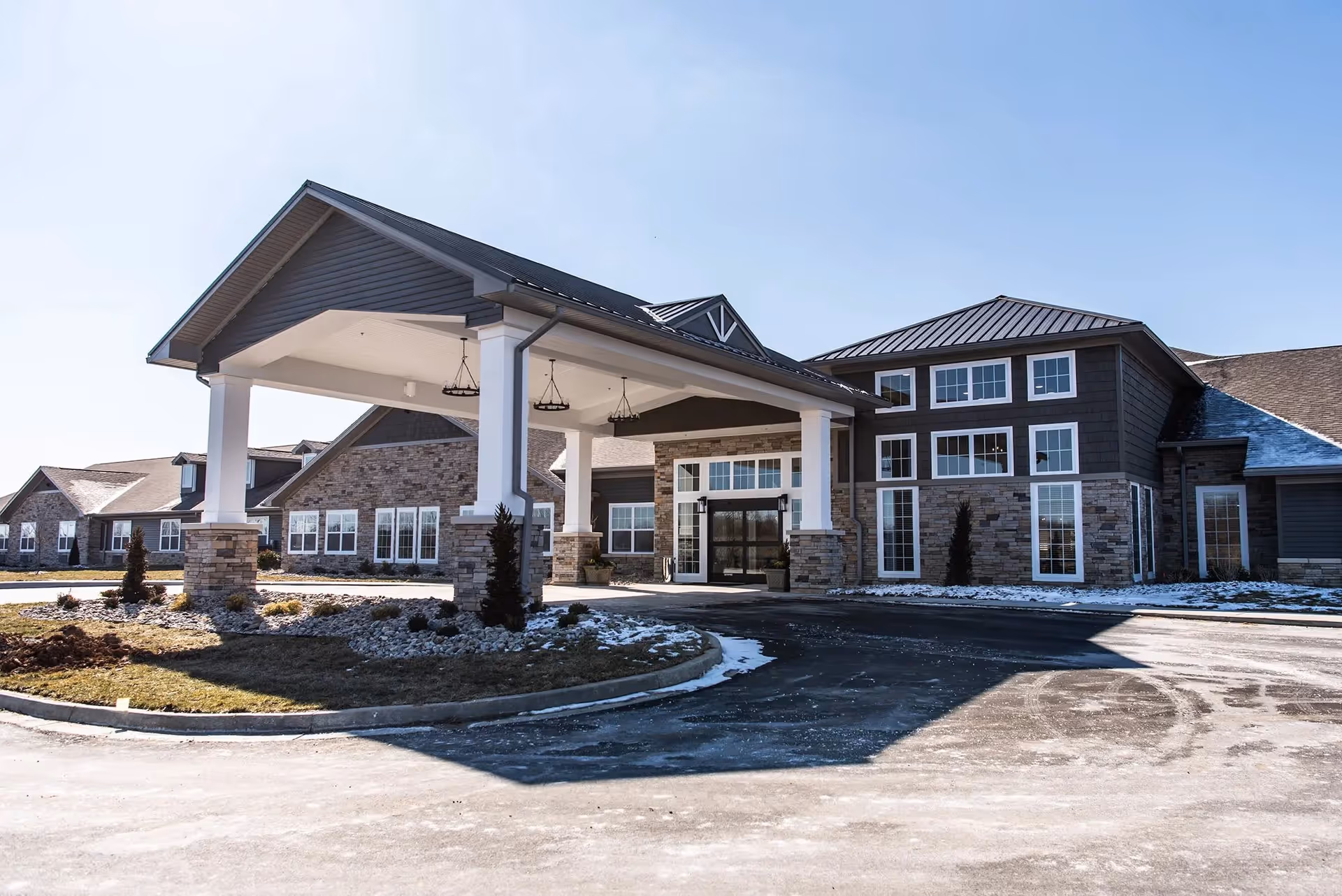 Exterior view of Charter Senior Living of Linden building with a covered entrance, stone and siding facade, multiple windows, and a driveway with some snow on the ground.