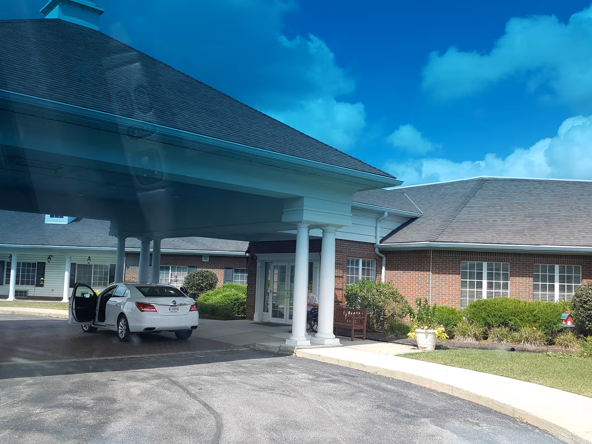 Brick senior living facility entrance with white columns and a parked car.