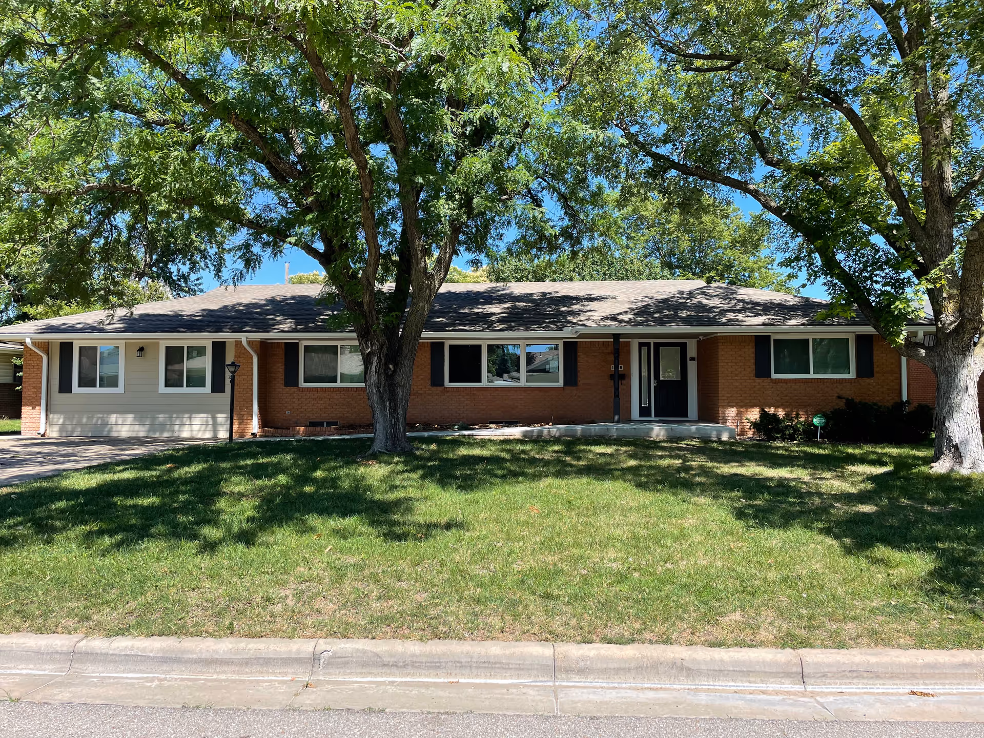 Single-story brick senior living building with a front entrance, two large trees, and lawn.
