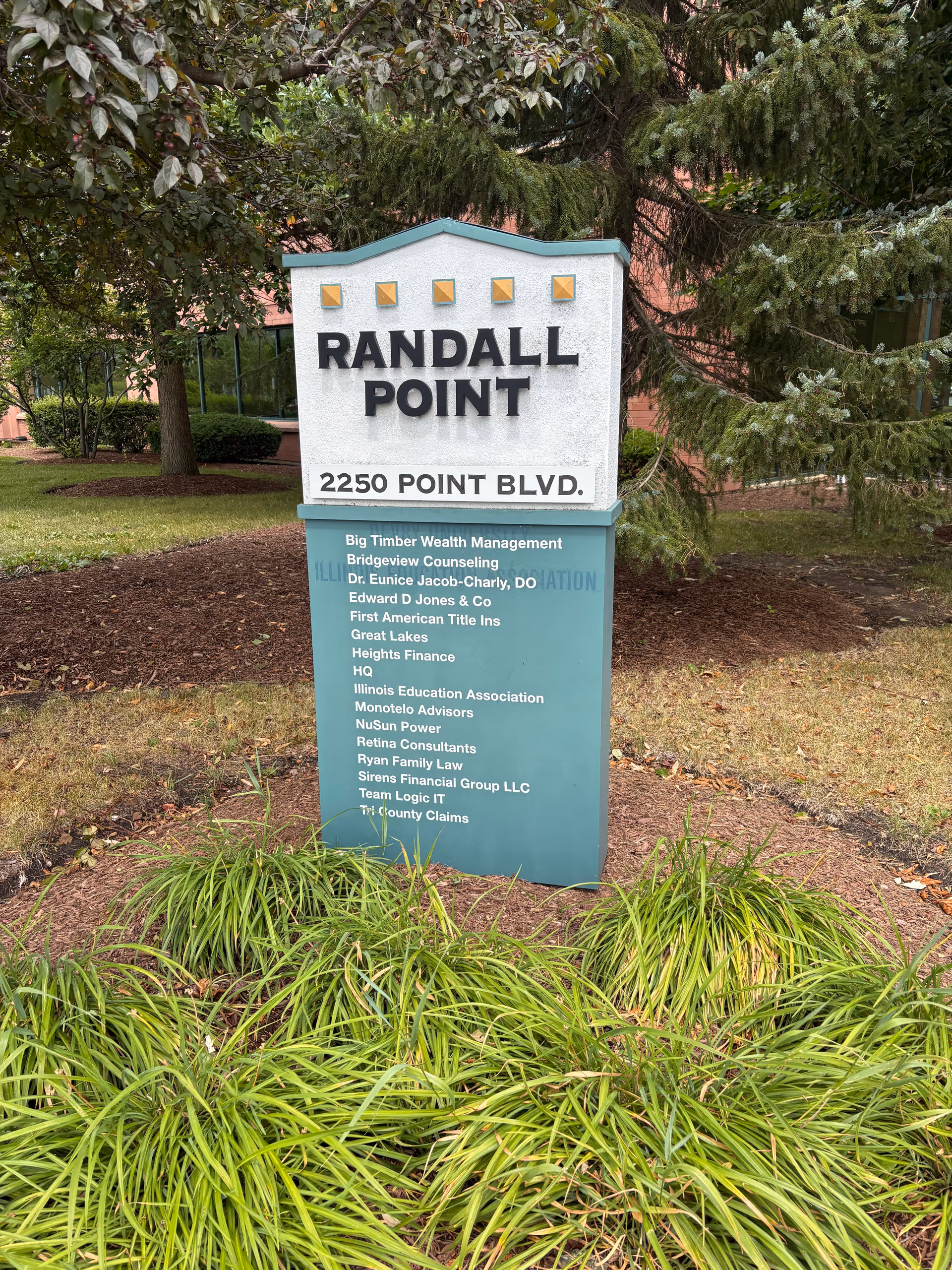 Outdoor sign reading RANDALL POINT at 2250 POINT BLVD amid shrubs.