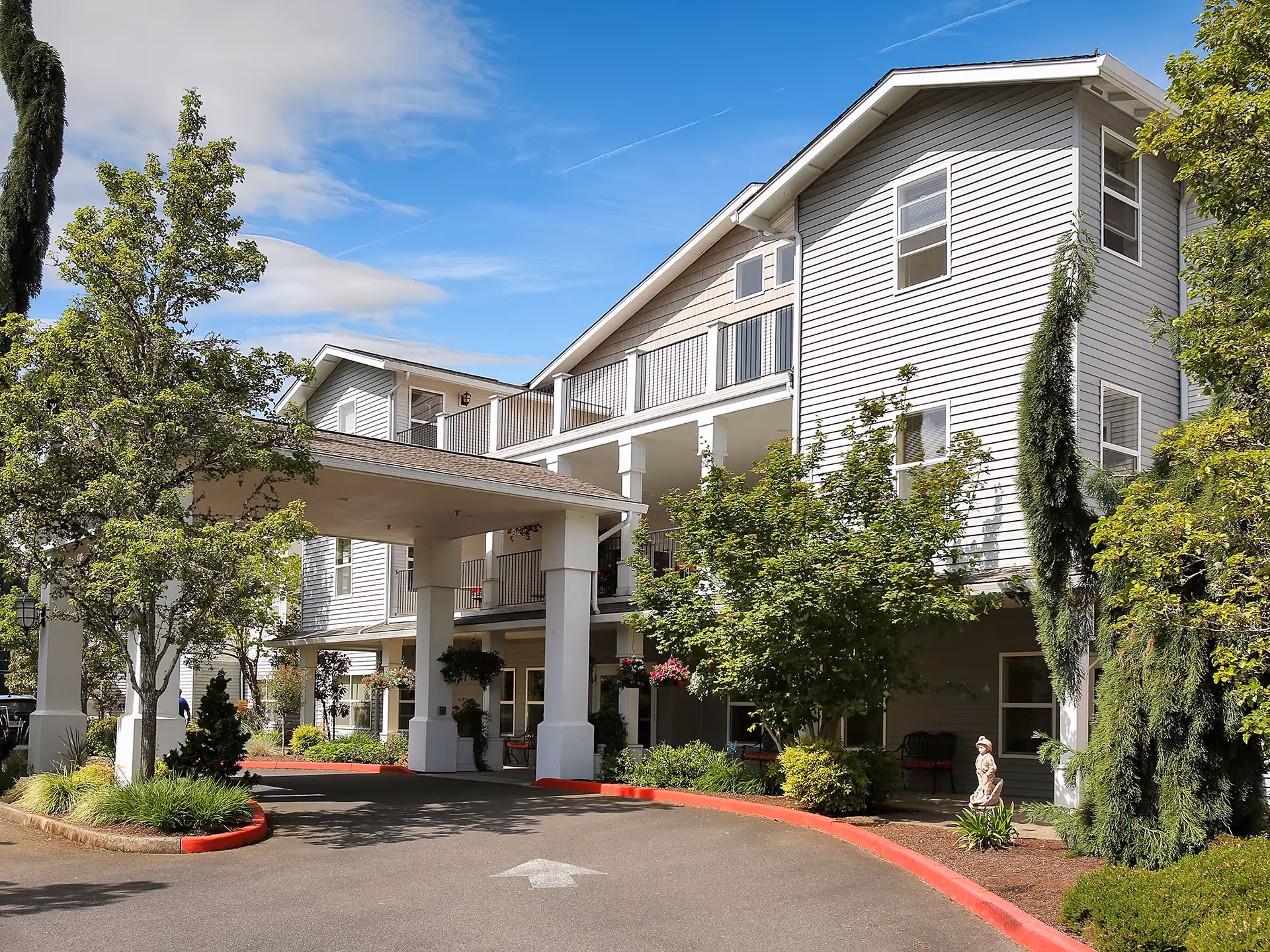 Two-story white senior living building with entrance canopy and landscaped grounds.