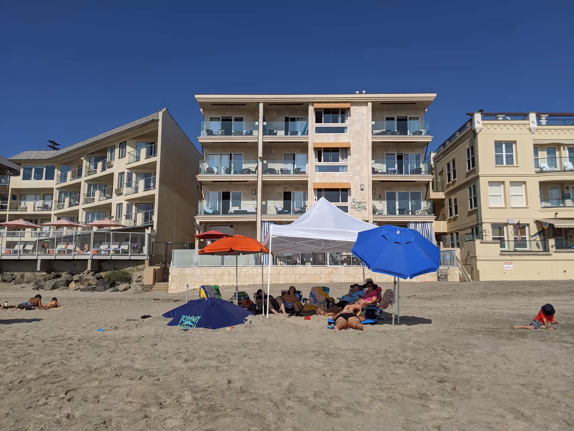 Beachfront view of a multi-story senior living building with beachgoers and umbrellas