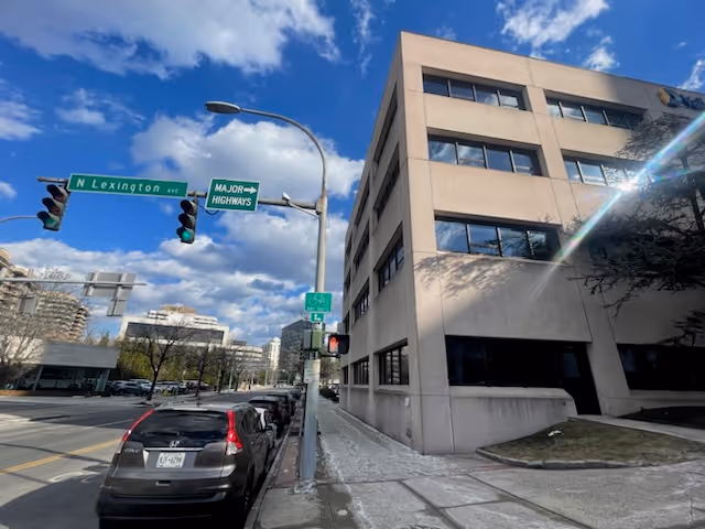 Exterior view of an office building on a city street with parked cars and traffic signals.