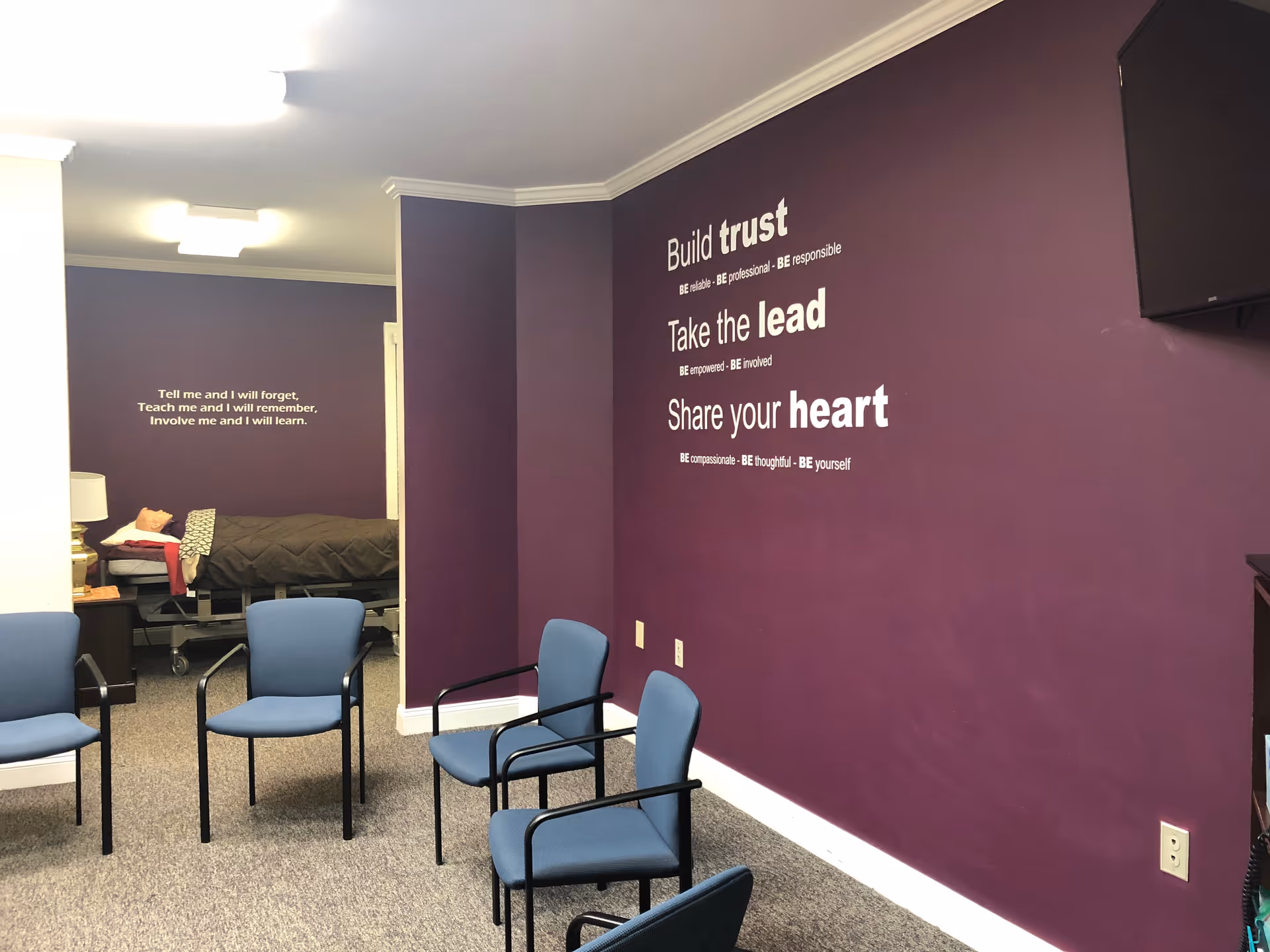 Purple-walled waiting area with blue chairs and a bed visible in the back.