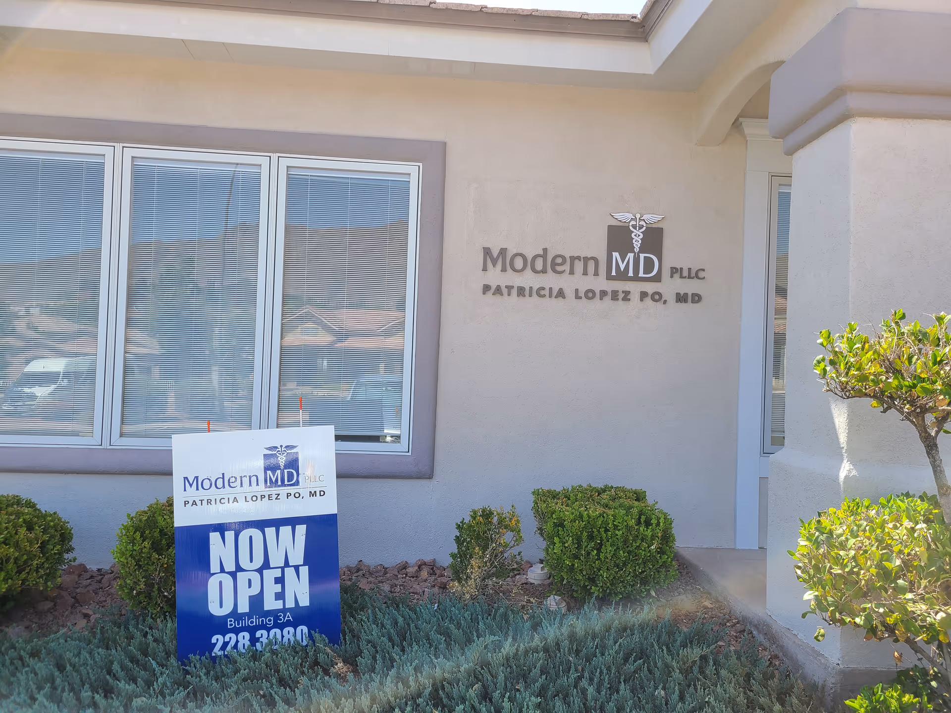 Front exterior of Modern MD clinic with sign and now open promotional board and landscaping.