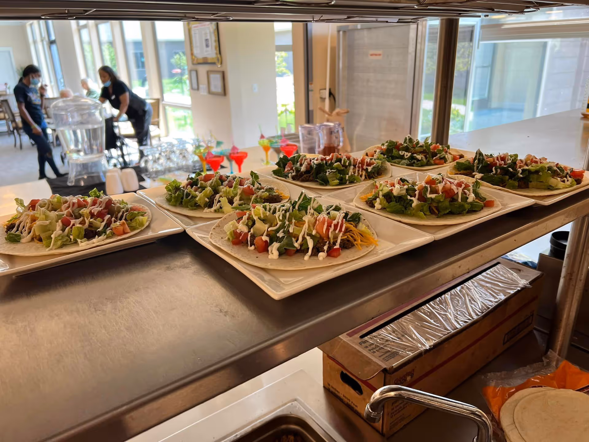 Plated salads arranged on a serving counter with staff in a bright dining area.