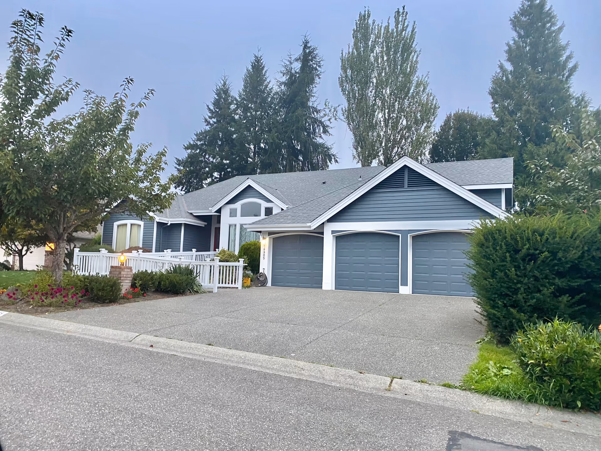 Blue, single-story home with a three-car garage and white railing near a landscaped yard.