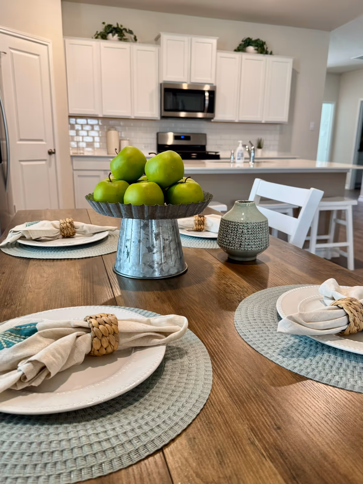 Dining table with plates and napkins, and a green apple centerpiece in a bright kitchen.