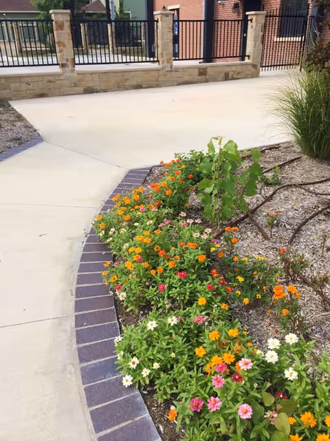 Curved sidewalk beside a colorful flower bed near a senior living facility exterior.