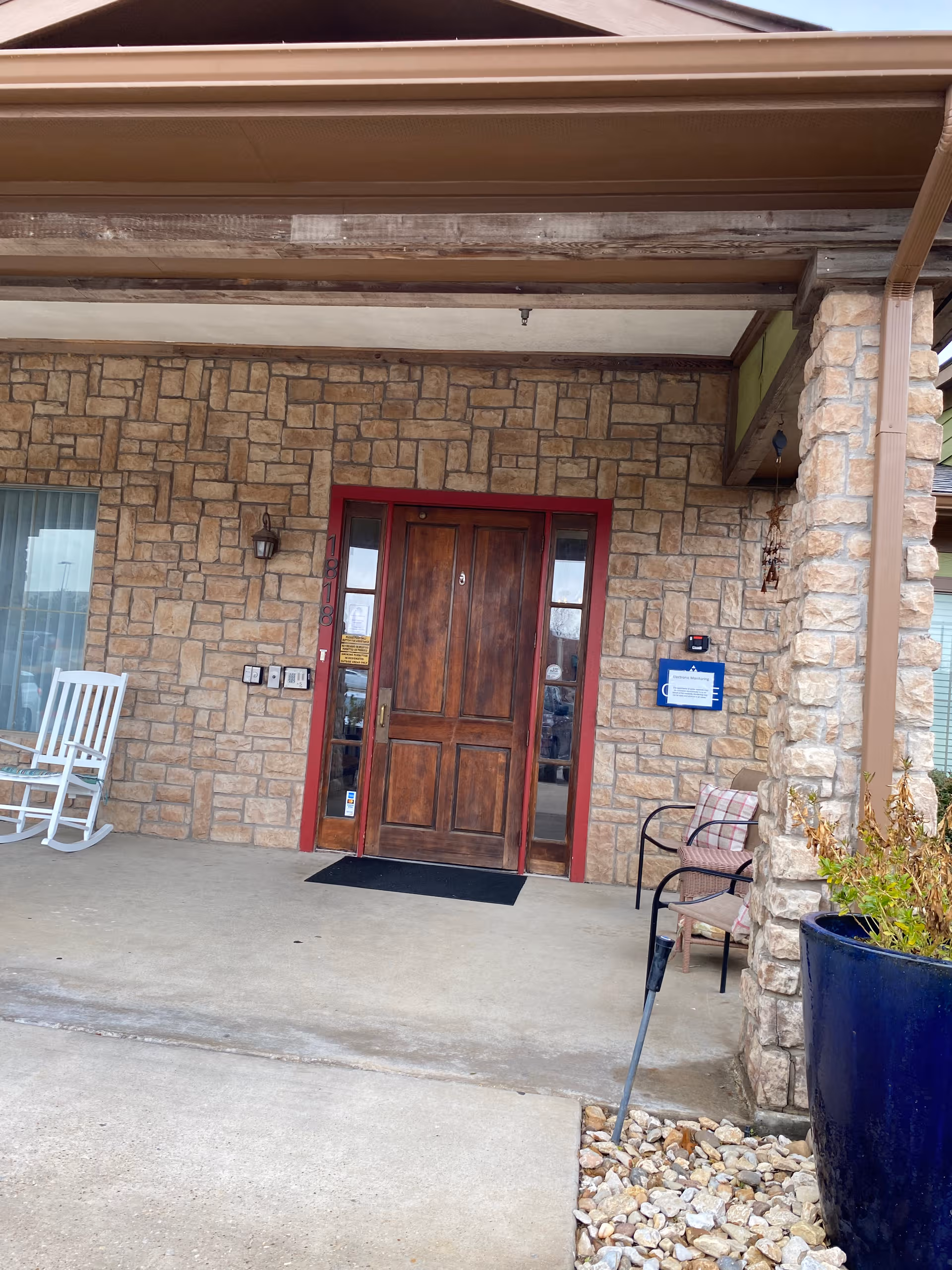 Entrance of a stone-clad senior living facility with wooden door and seating.
