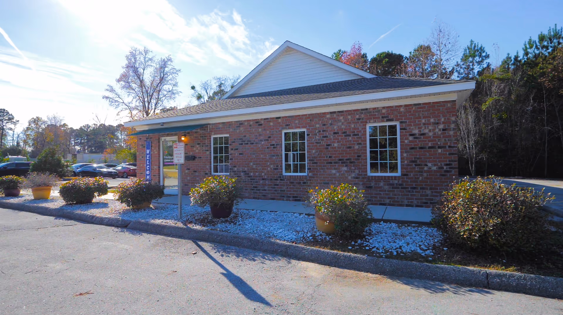Brick facility building with a welcome sign, front landscaping, and parked cars.