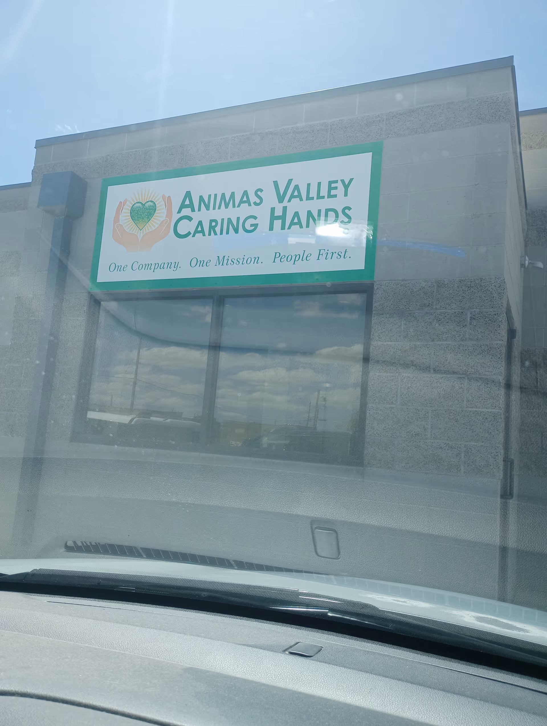 Exterior view of Animas Valley Caring Hands sign on building facade, reflected in glass.