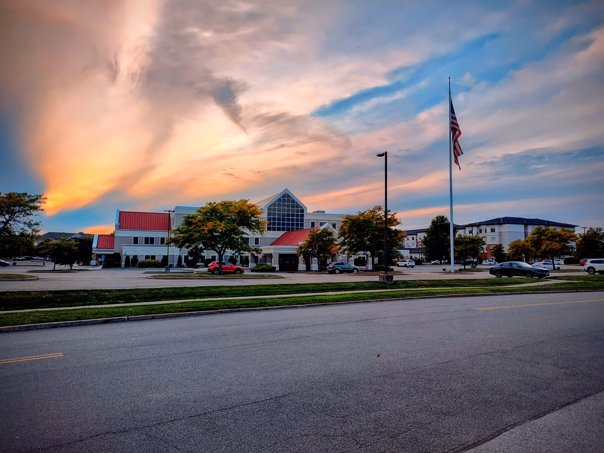 Sunset over a medical building's front, with trees, flagpole, and a parking area.
