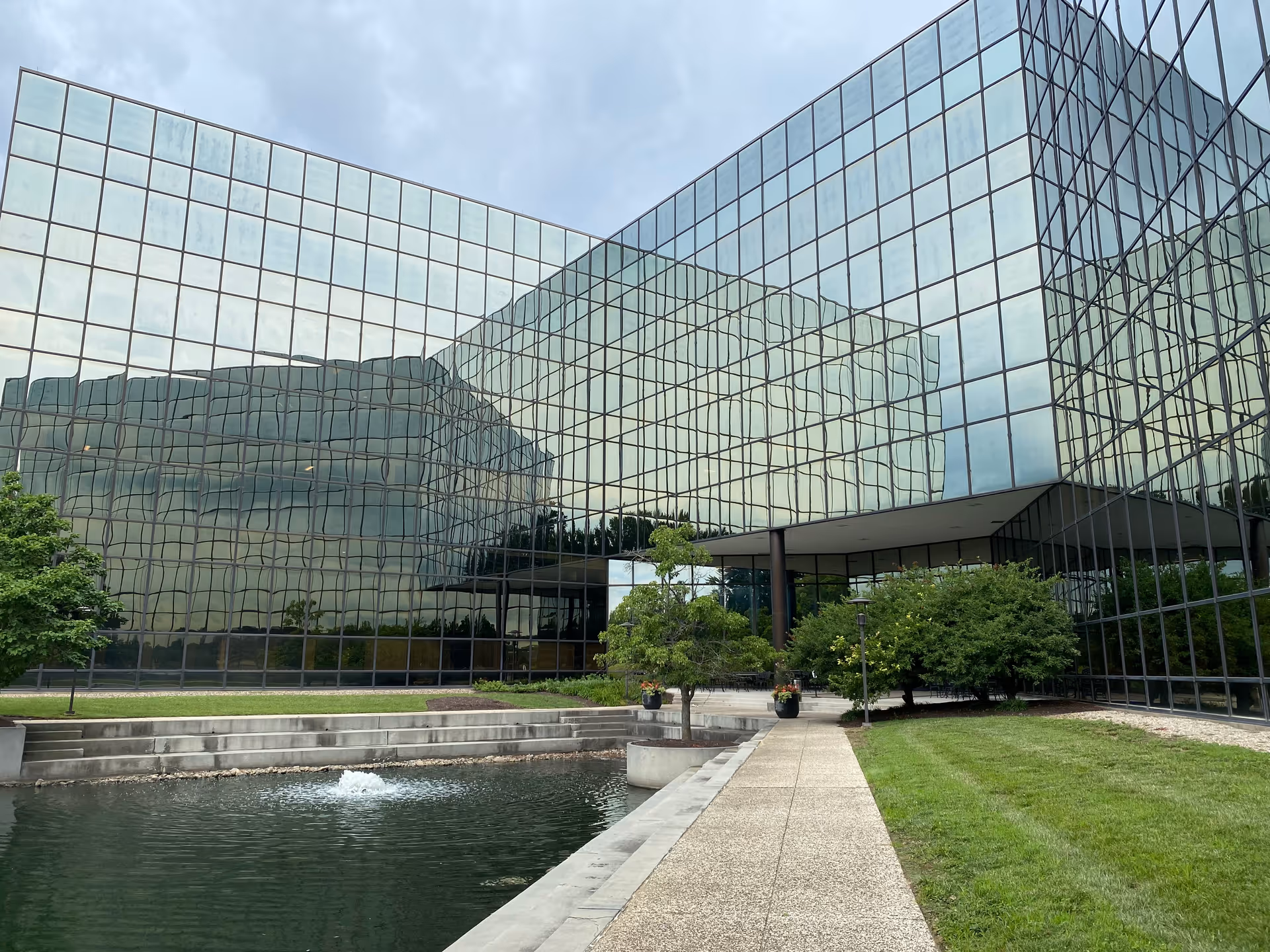 Modern glass building with reflecting facade, walkway, and surrounding greenery.