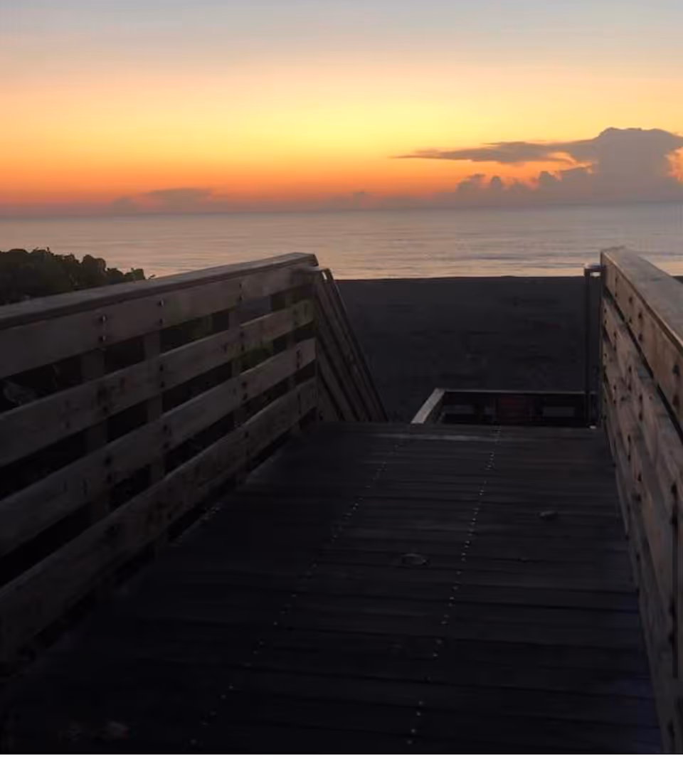 Sunset over the ocean seen from a wooden boardwalk railing by the beach