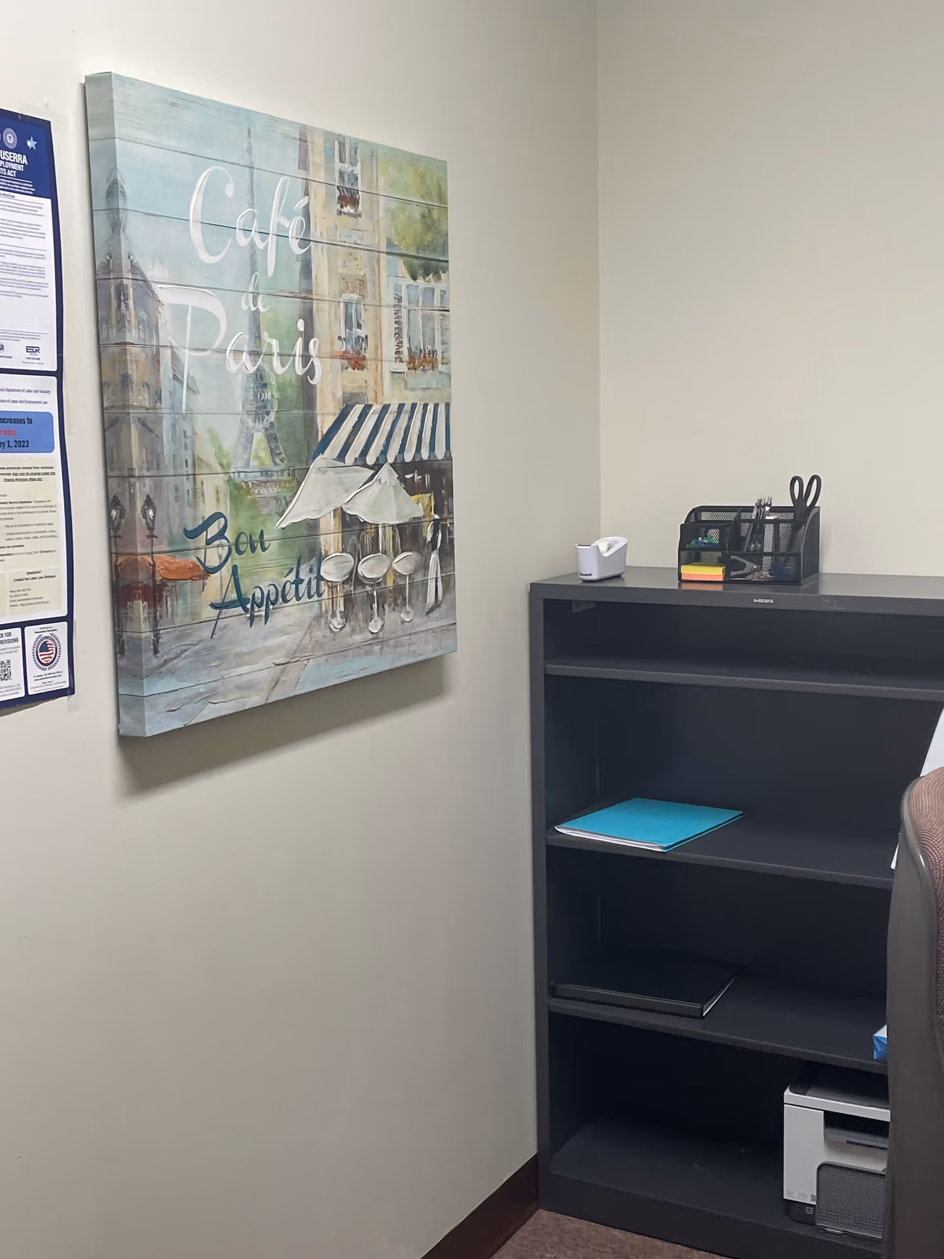 A small office corner featuring wall art and a tall black shelving unit.