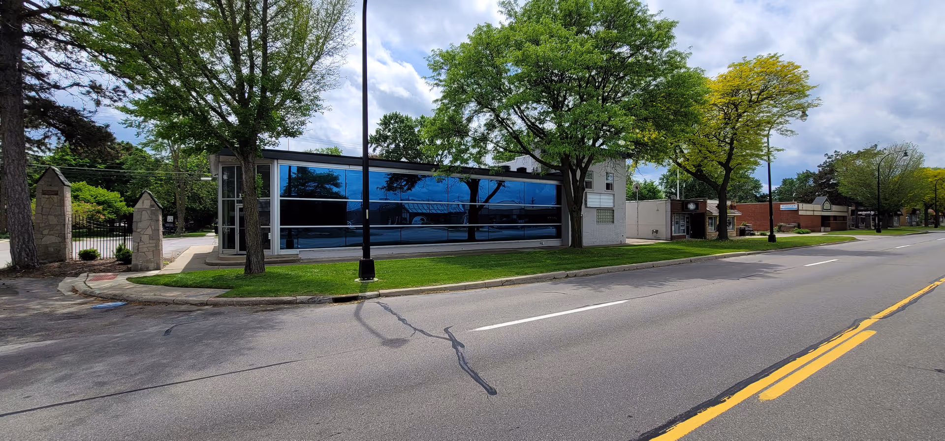 Modern glass-front senior care building along a tree-lined street with green lawn