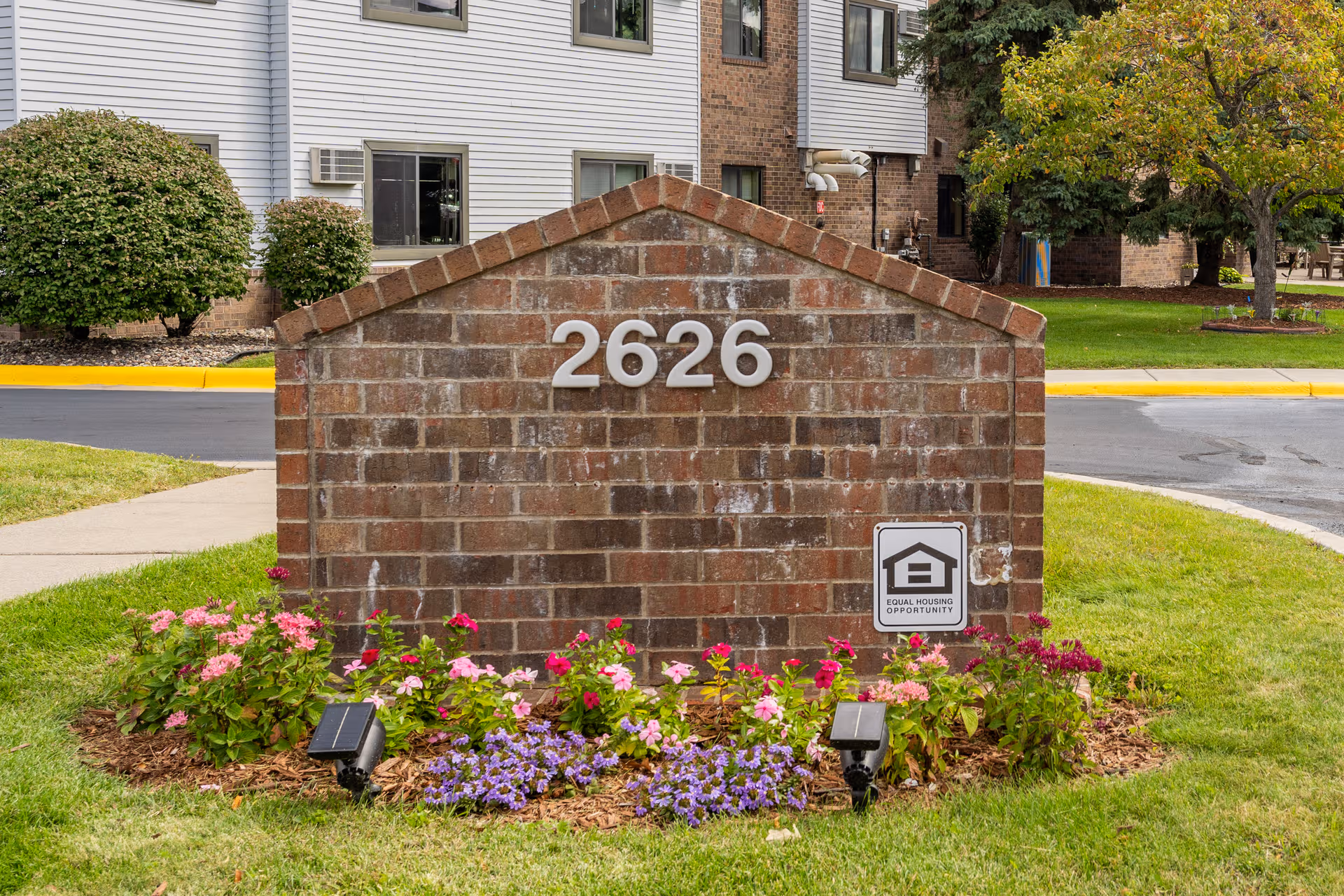Brick sign with the number 2626 sits in front of a building, surrounded by flowers.