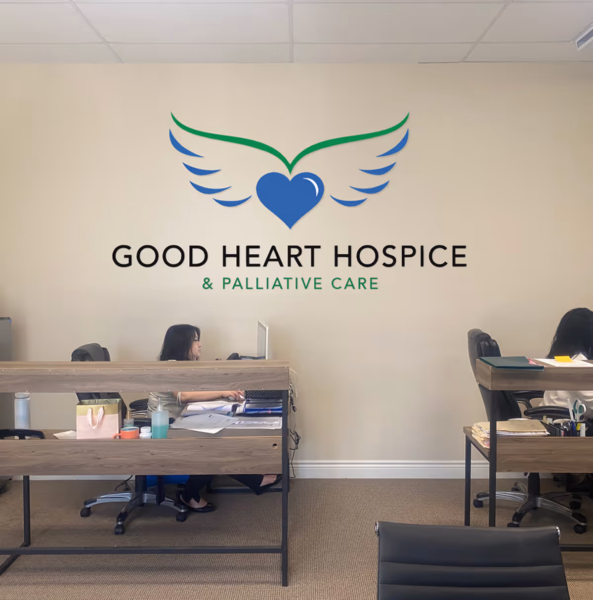 Reception area inside a hospice office with desks and a large Good Heart Hospice sign.