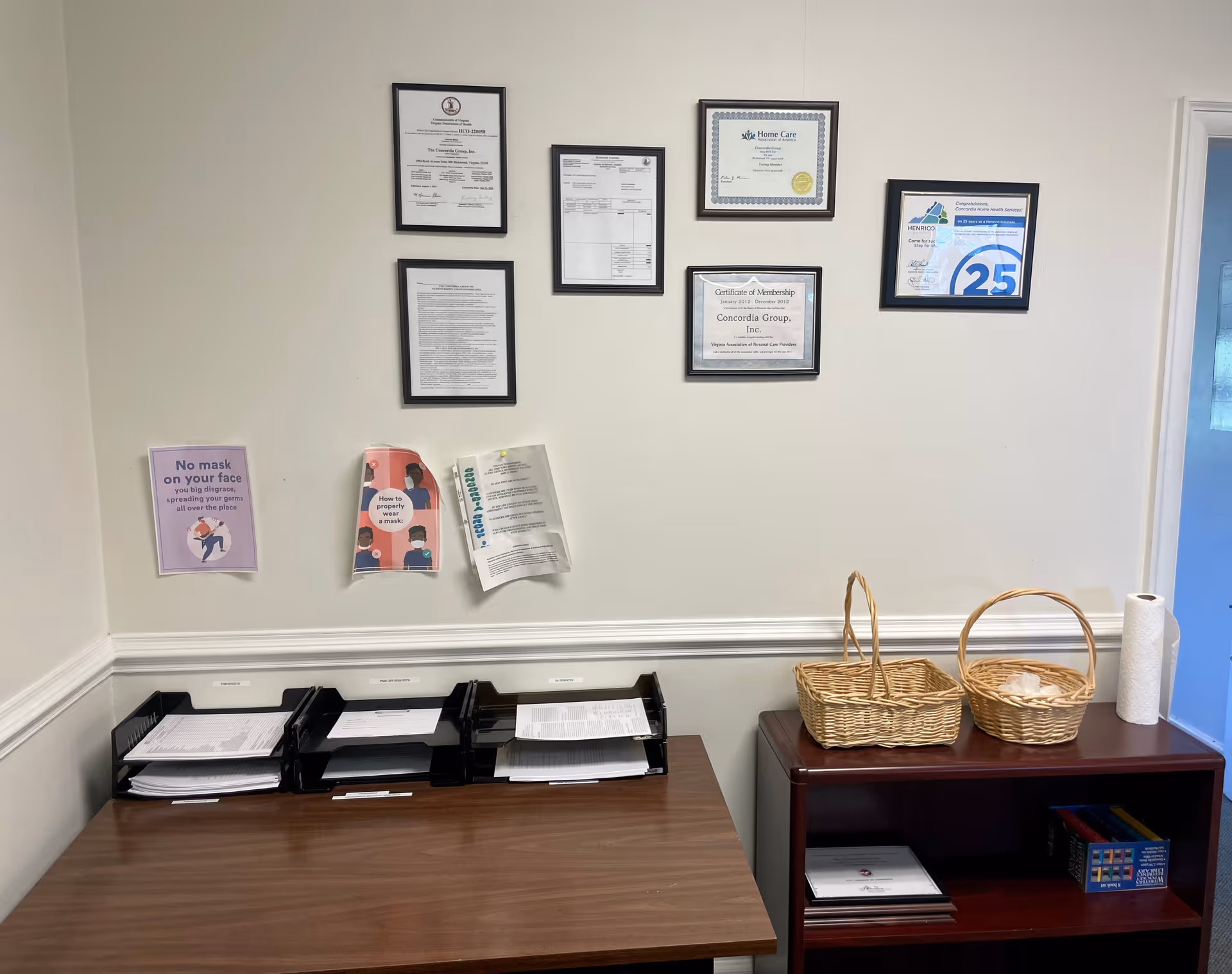 Office corner inside a senior facility with framed certificates, a desk, and wicker baskets.