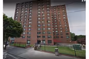 Tall brick senior living center exterior with a fenced lawn and sidewalk
