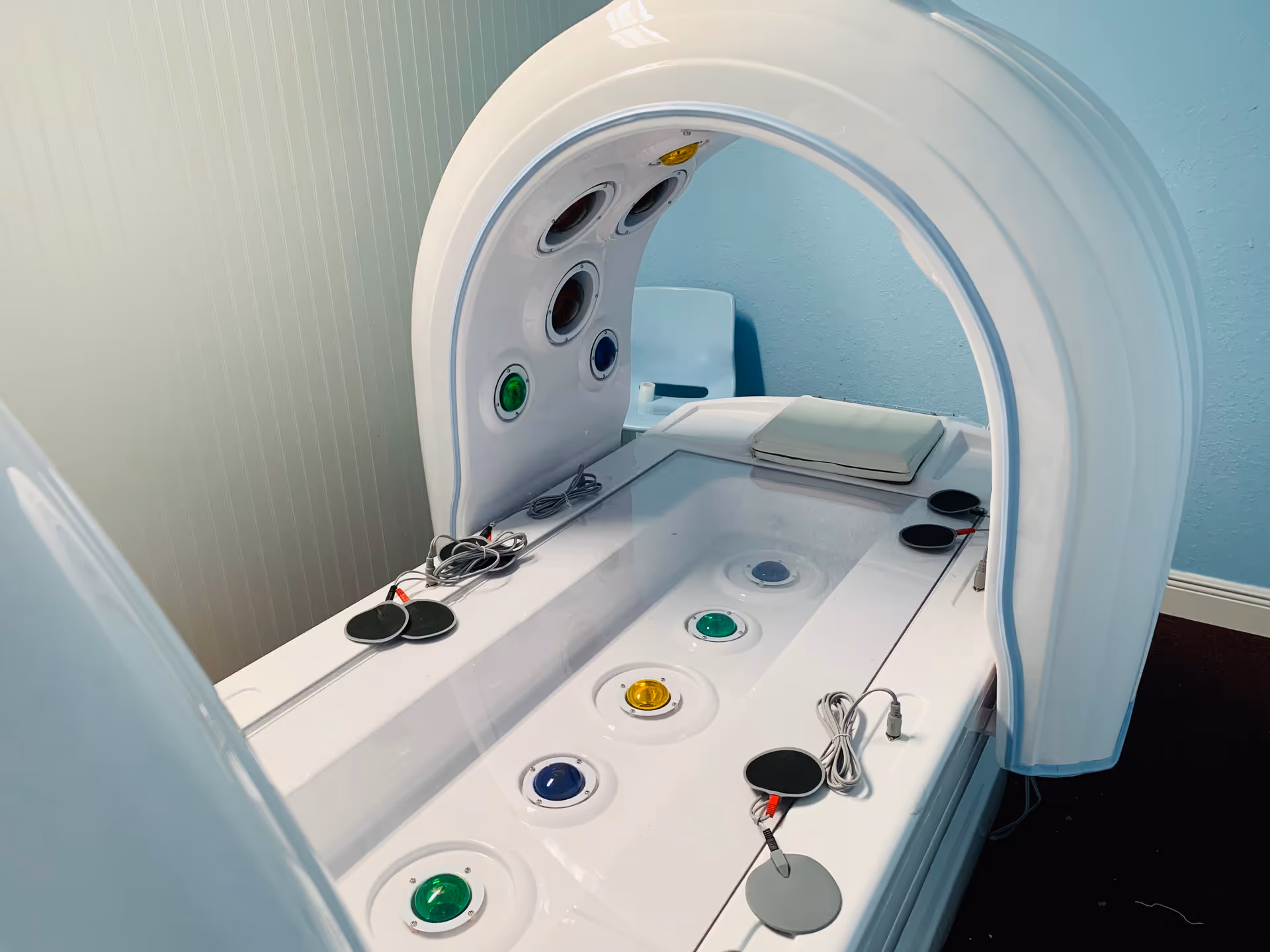 A large white circular imaging machine with a patient bed in a pale blue treatment room.
