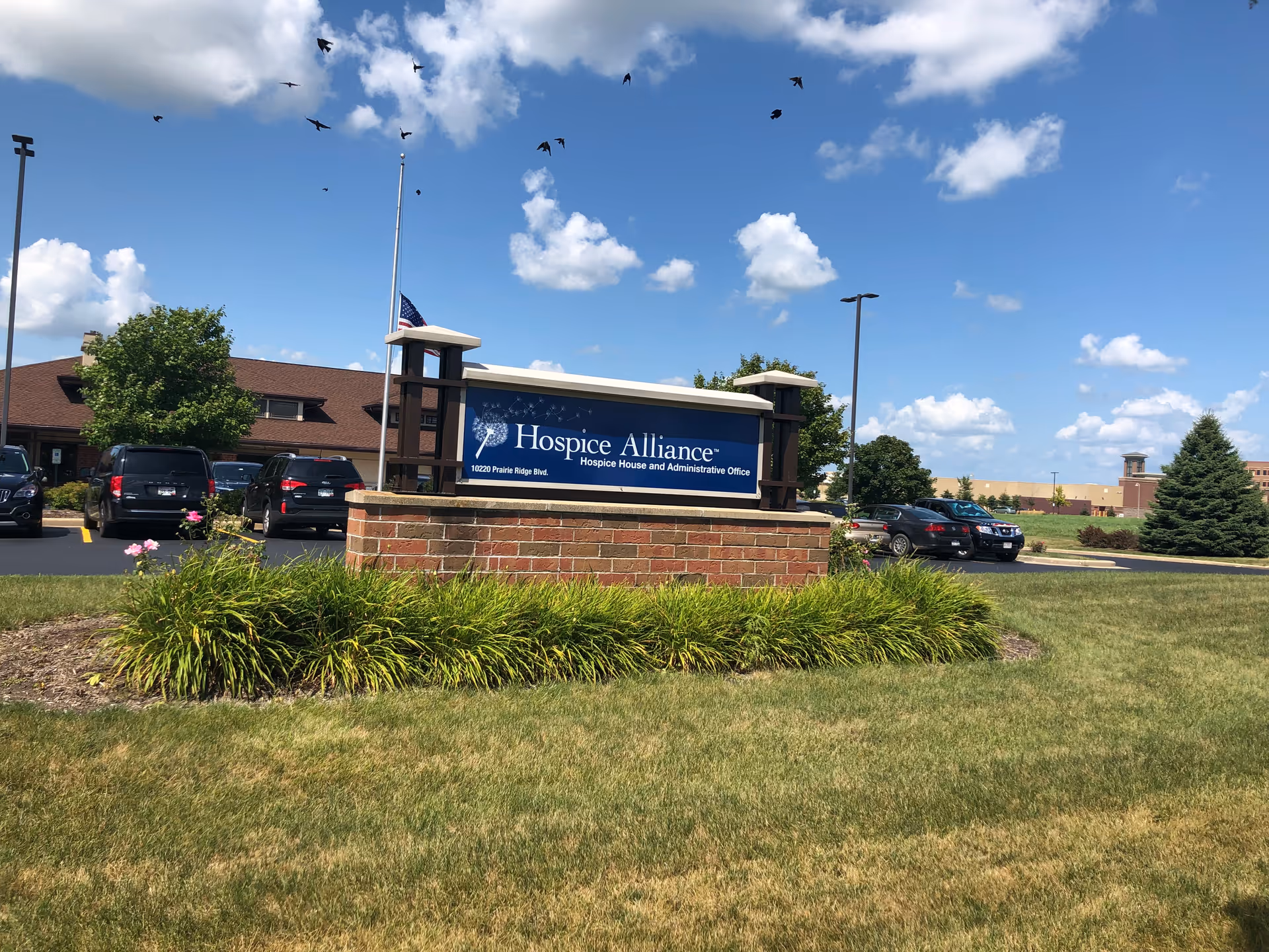 Outdoor view of Hospice Alliance sign with brick base and surrounding landscaping.