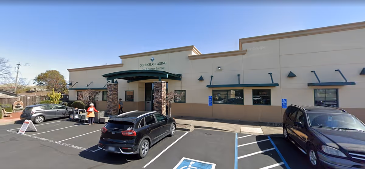 Exterior view of a beige Council on Aging building with a covered entrance and parked cars.