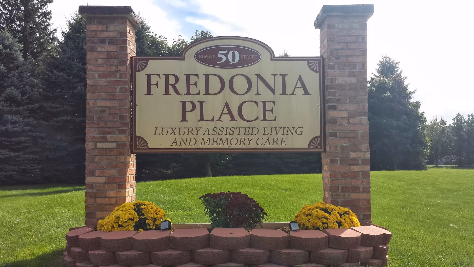A Fredonia Place sign on brick pillars framed by a green lawn.