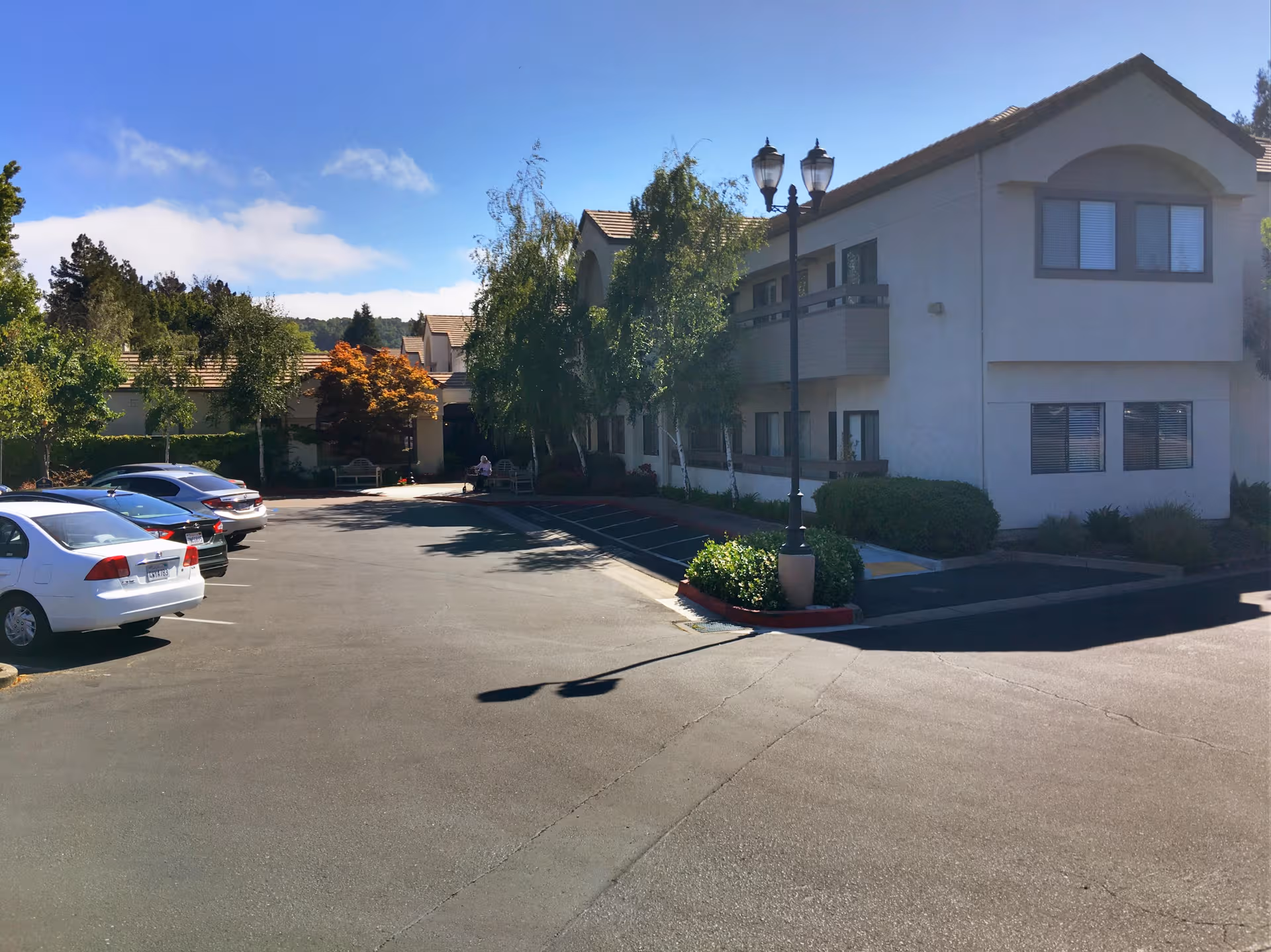 Two-story senior living facility with beige exterior, parking lot, and a streetlamp in front.