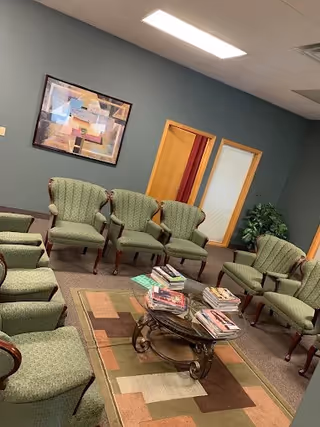 Senior living facility lounge with green upholstered chairs arranged around a central coffee table.