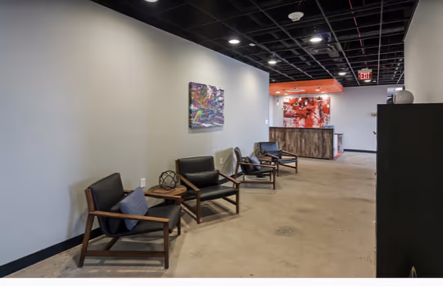 A spacious lobby area with black chairs, wall art, and a reception desk in back.
