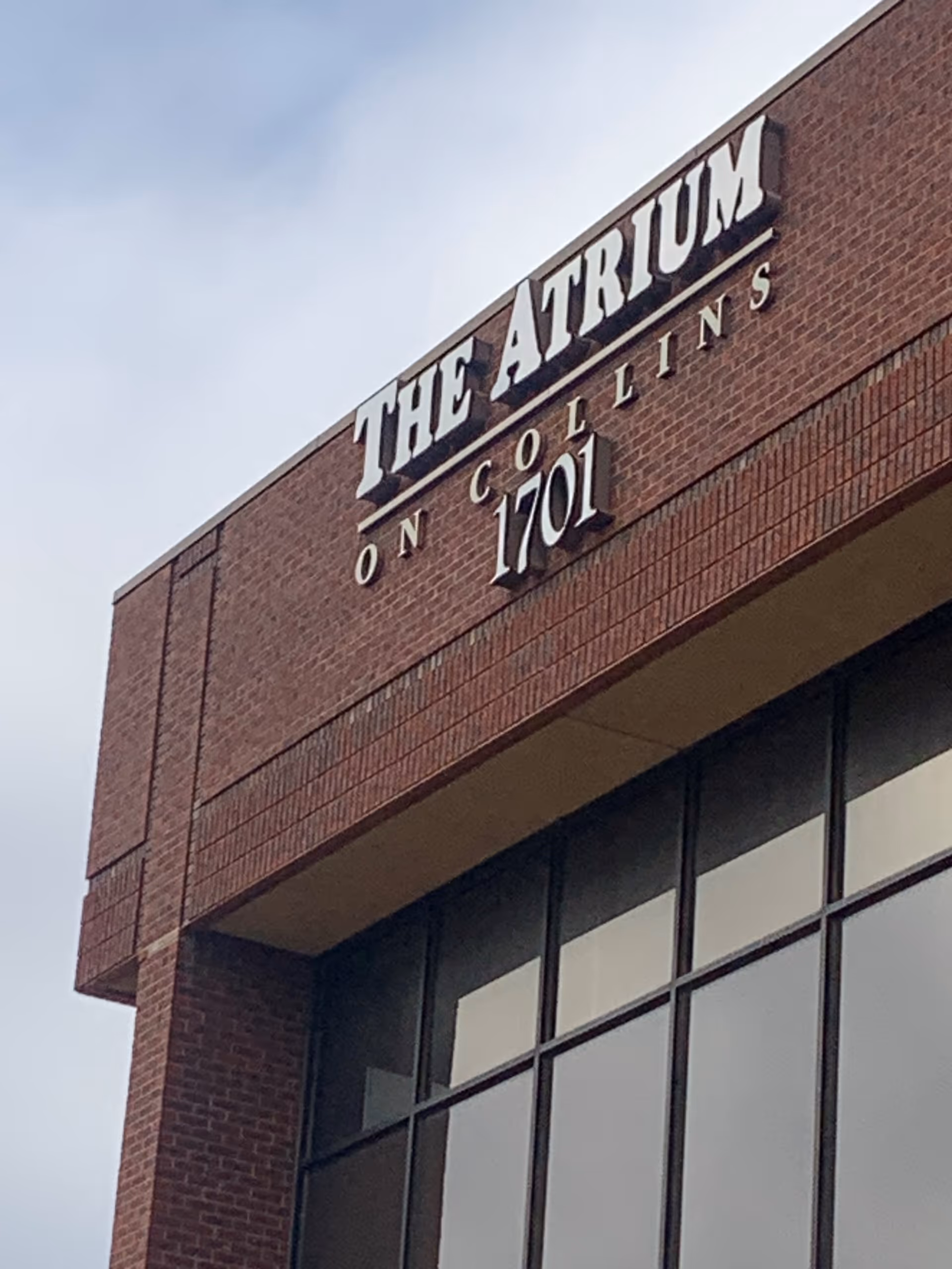 Brick building exterior with large sign reading THE ATRIUM ON COLLINS over windows.