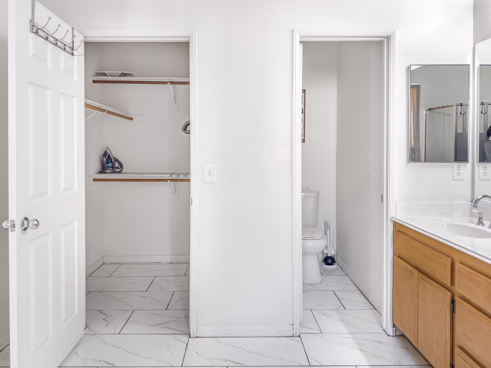 Bright bathroom area with toilet partition, closet space, and wooden vanity.