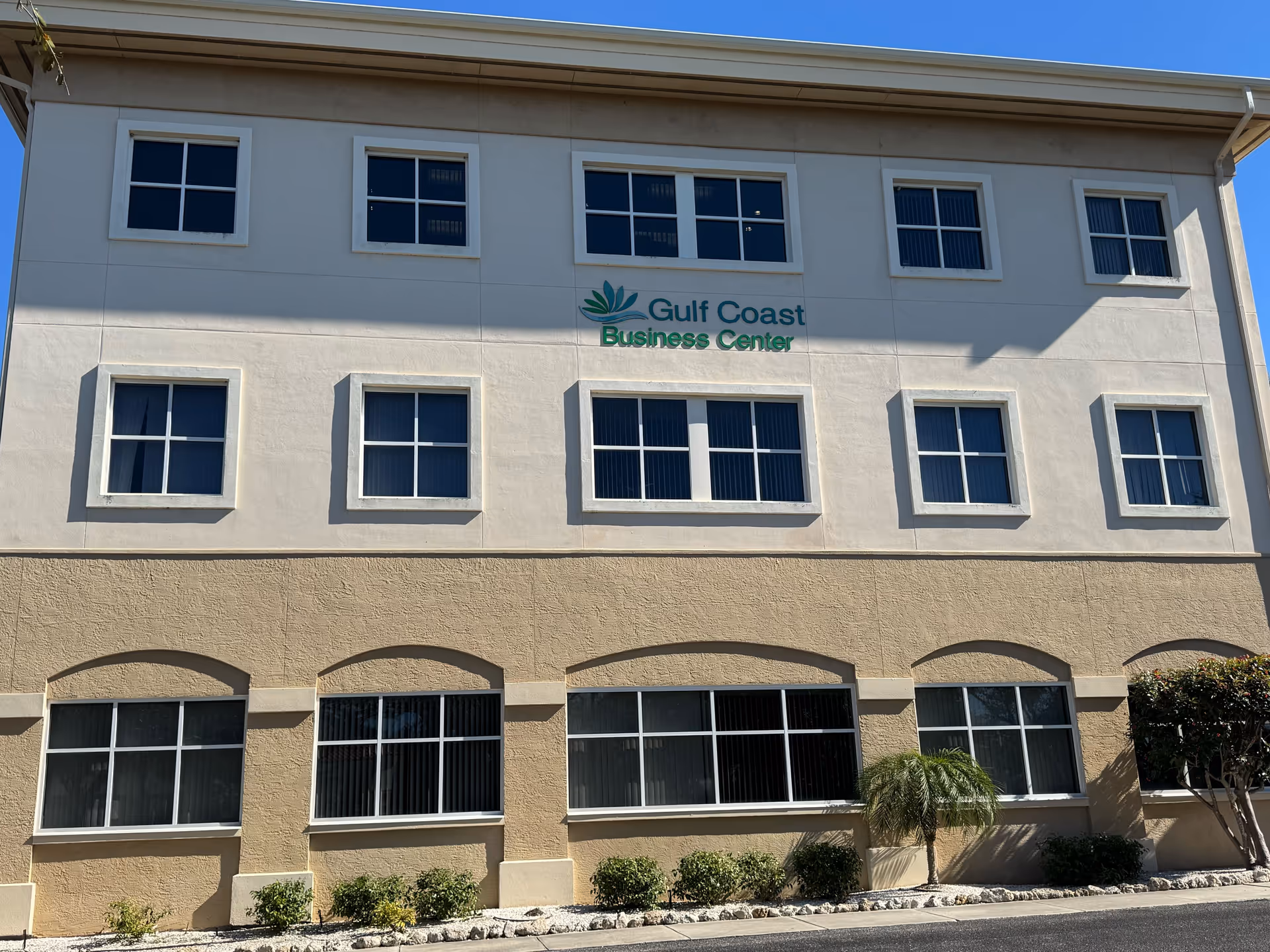 Three-story beige commercial building with multiple windows and a Gulf Coast Business Center sign.