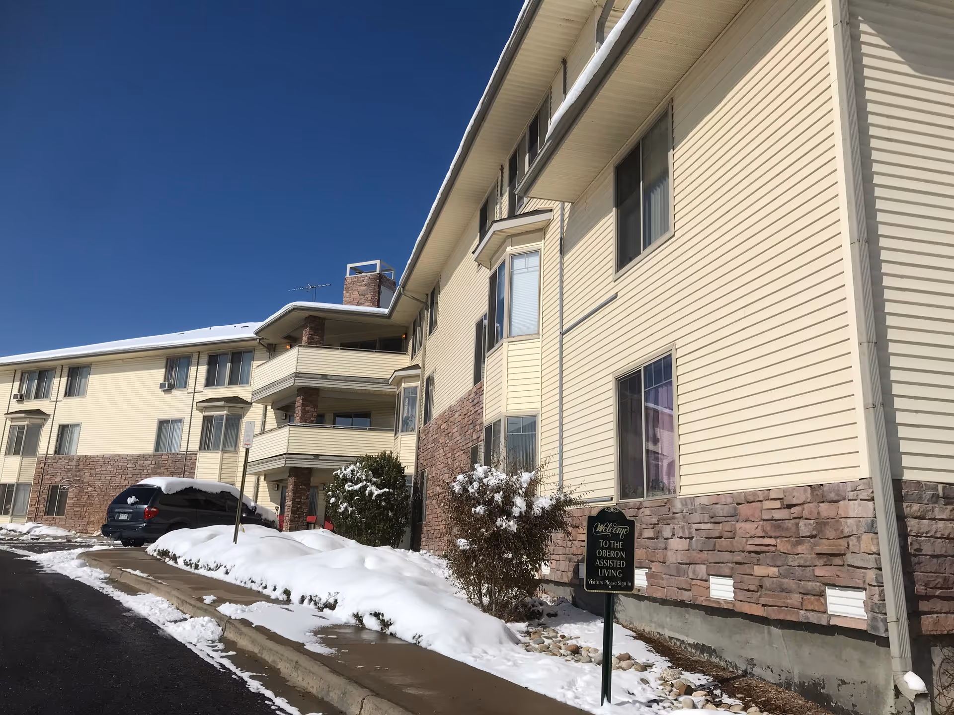 Exterior view of a beige senior living building with stone accents and snow.