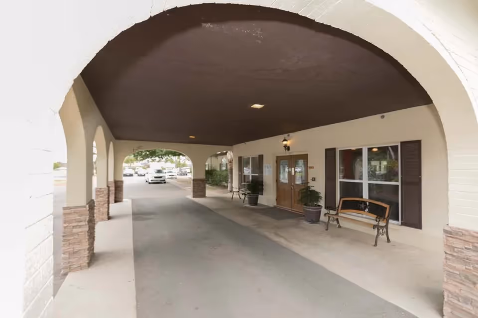 Covered archway entrance of Village Healthcare and Rehabilitation with benches and plants.
